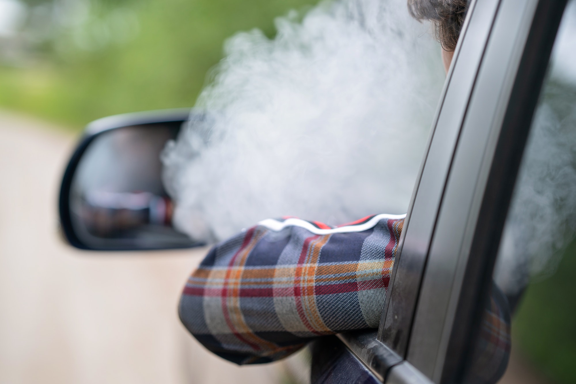 a young man sits behind the wheel in a car and smokes an electronic cigarette